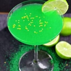 green martini in a martini glass with a lime on the edge and star sprinkles on top.