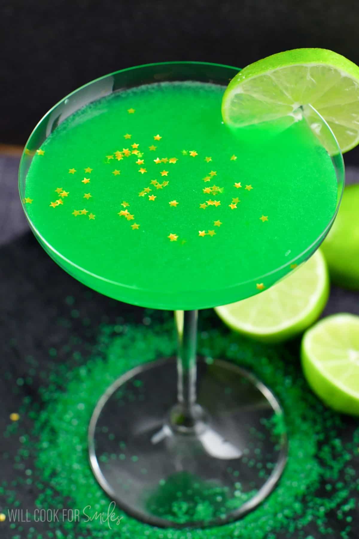 Lime martini in a martini glas with a lime on the edge of the glass and gold stars sprinkles on top.