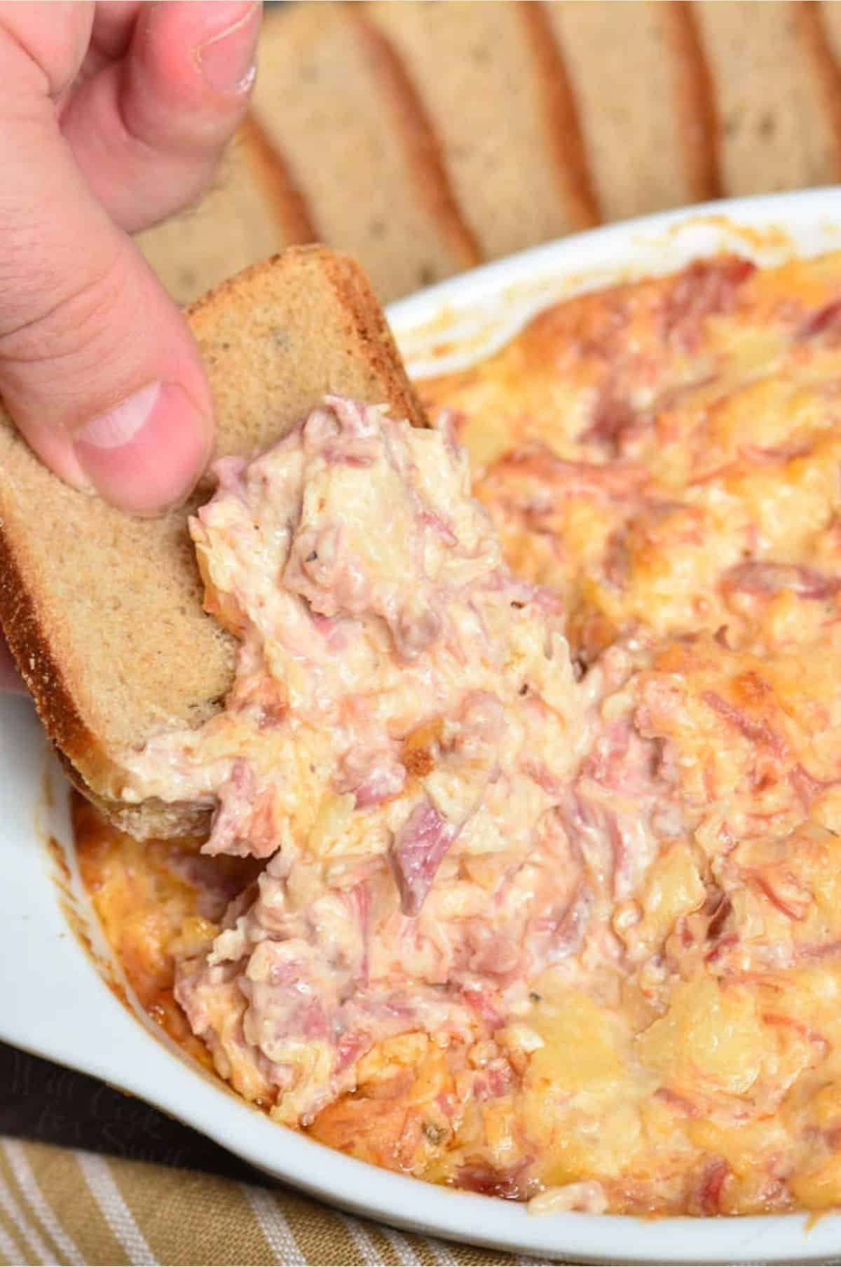 Scooping up some Reuben dip onto a piece of bread.