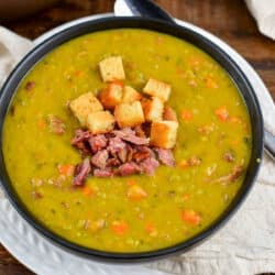 split pea soup in a black bowl with croutons and some ham on top.