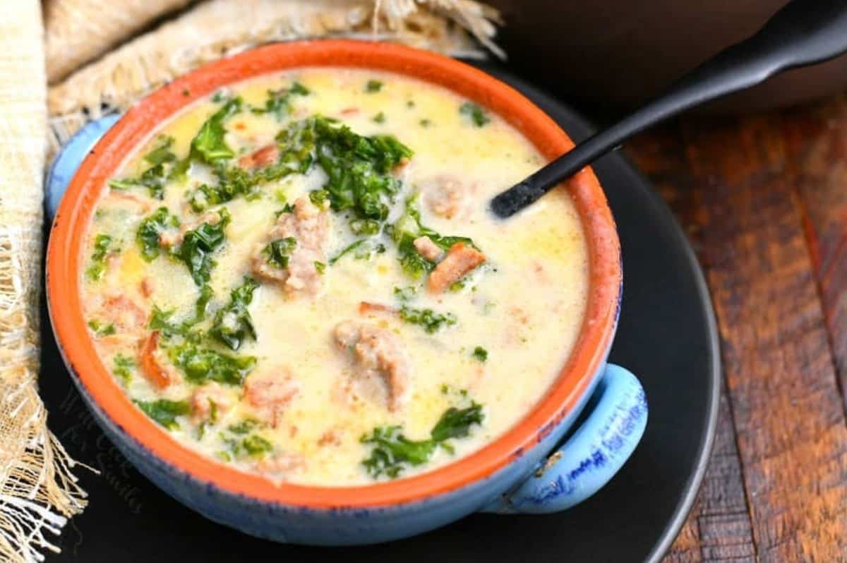 Zuppa Toscana soup in a bowl on a plate with a spoon to the right.