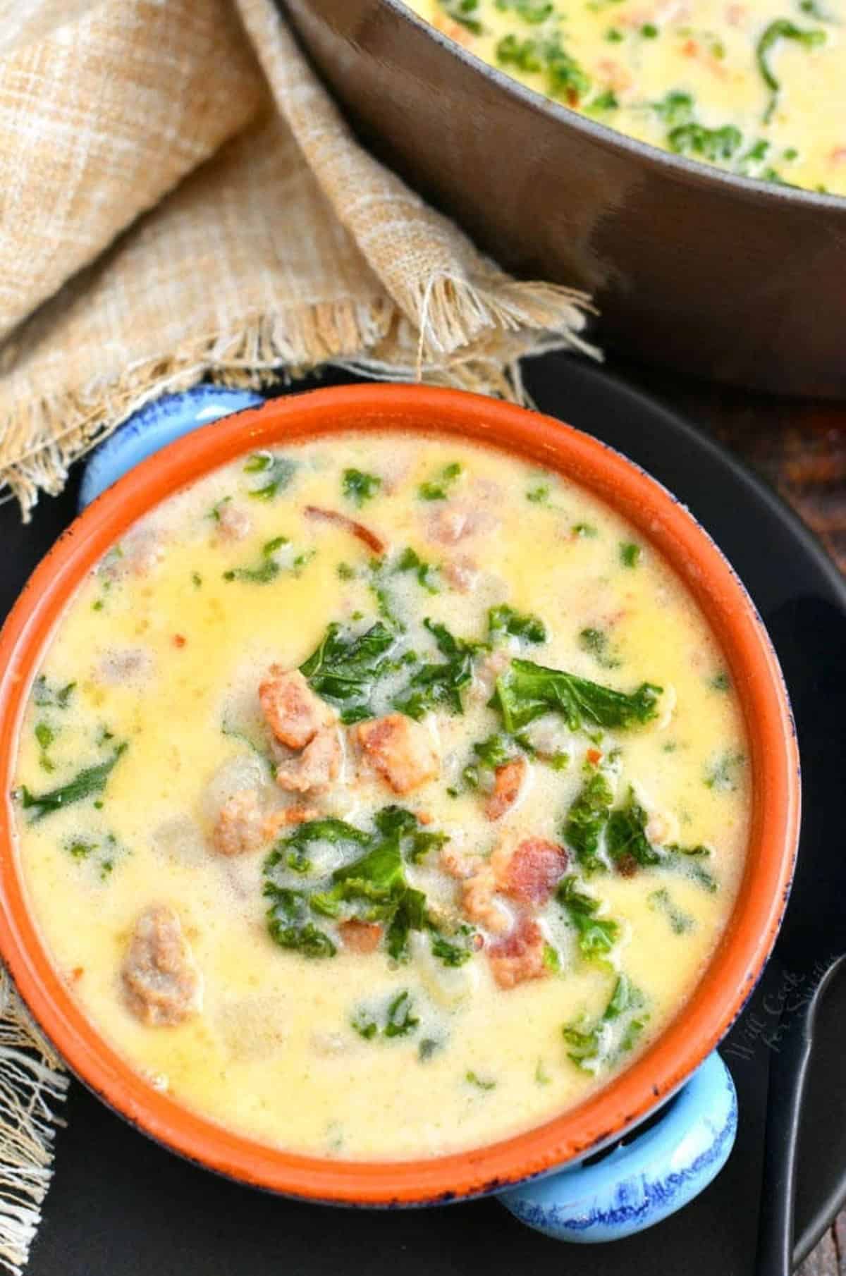 A bowl of zuppa Toscana soup on a black plate.