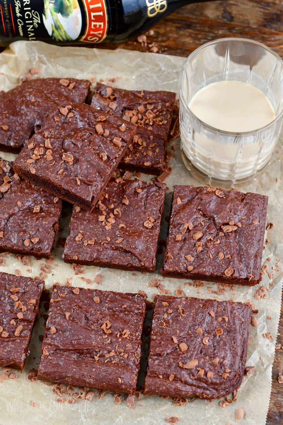 Bailys brownies cut into squares on a piece of parchment paper with a glass with baileys in it.
