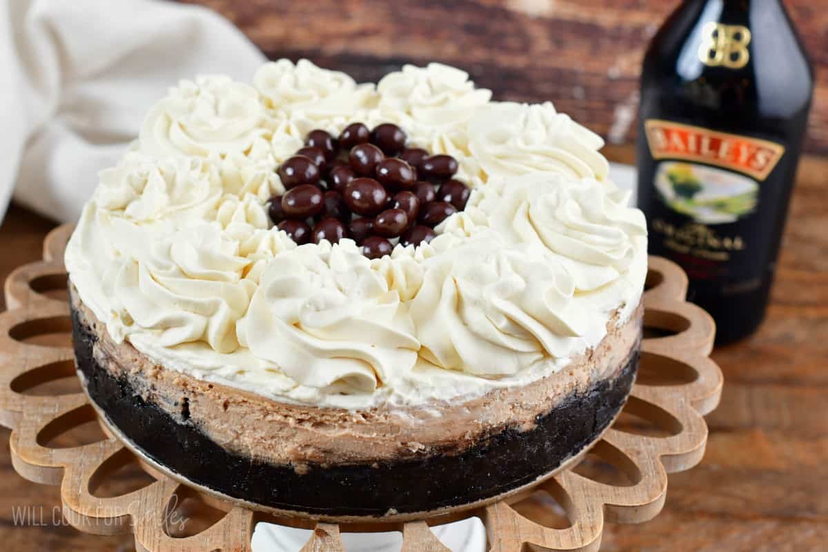 Bailey's cheesecake on a stand decorated with Bailey's whipped cream and chocolate espresso beans.