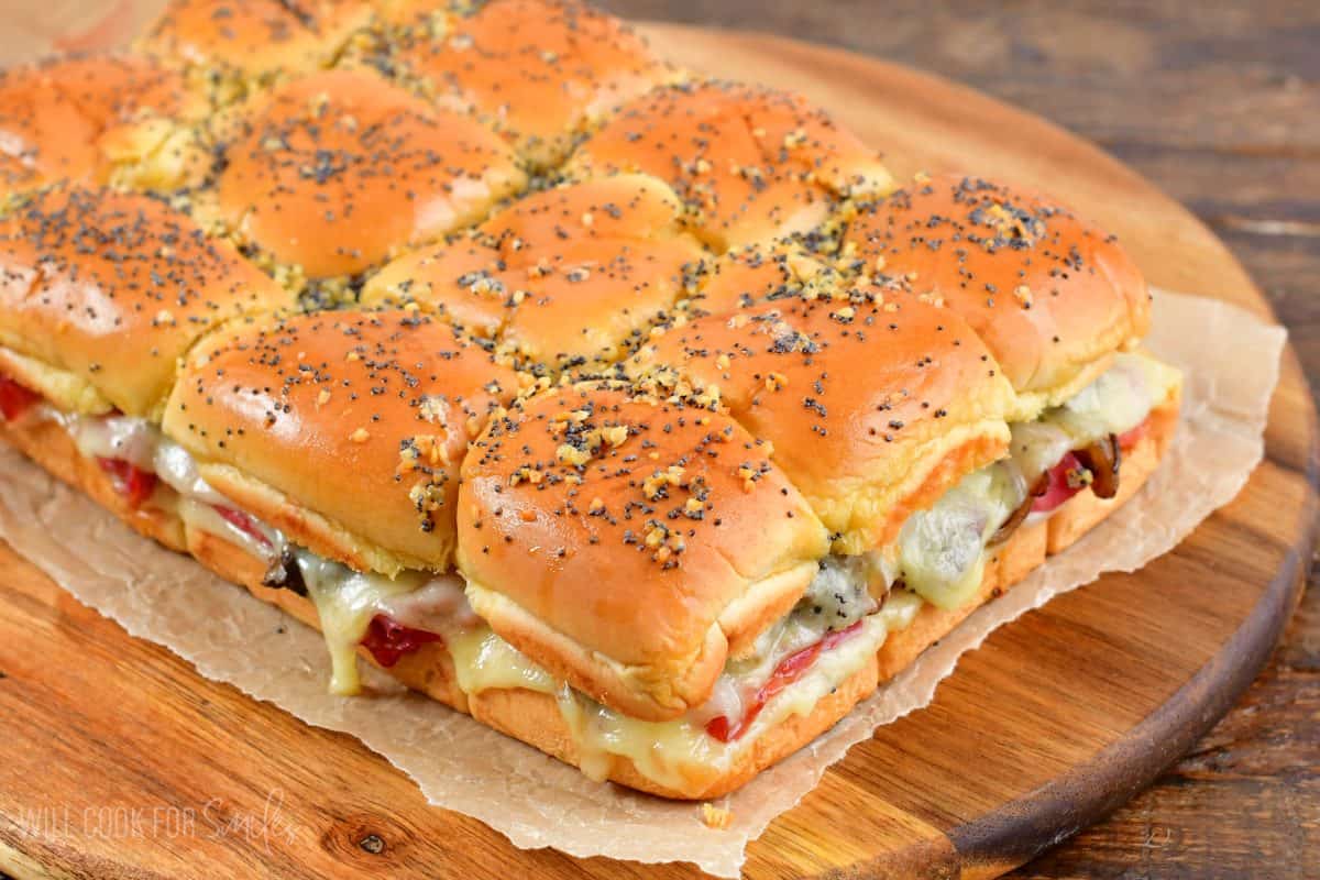 baked corned beef sliders on a piece of wax paper on a wood cutting board.