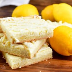 lemon cheesecake cookie bars on a wood surface with lemons around them.