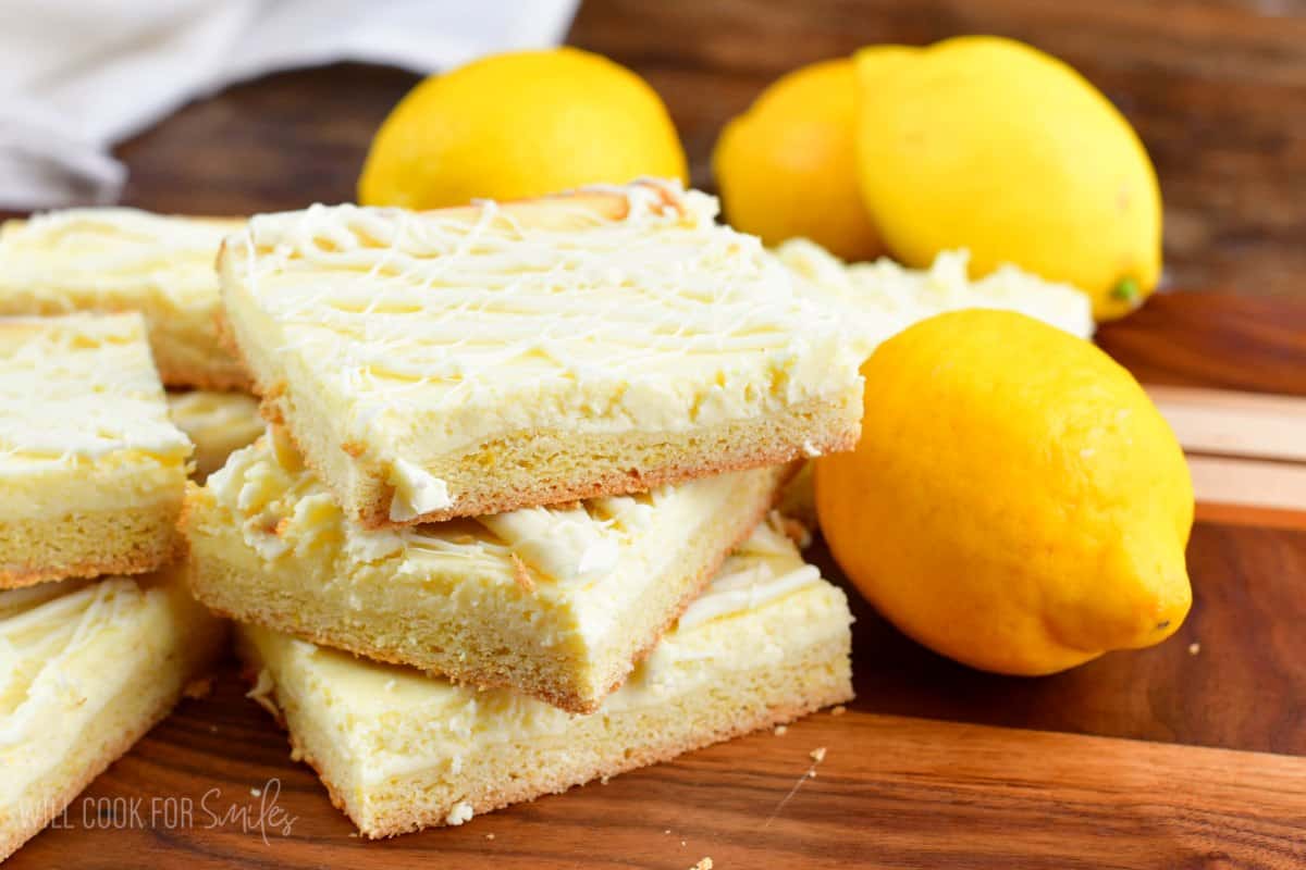 lemon cheesecake cookie bars on a wood surface with lemons around them.