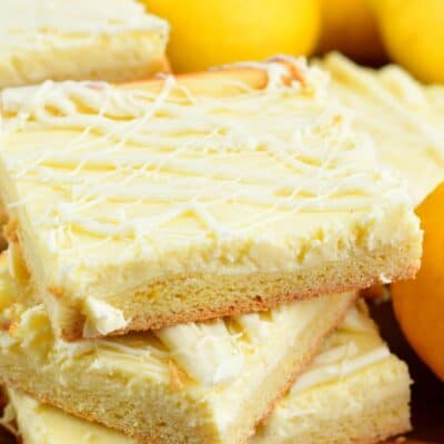 Lemon Cheesecake Cookie bars stacked up on top of each other on a wood cutting board.