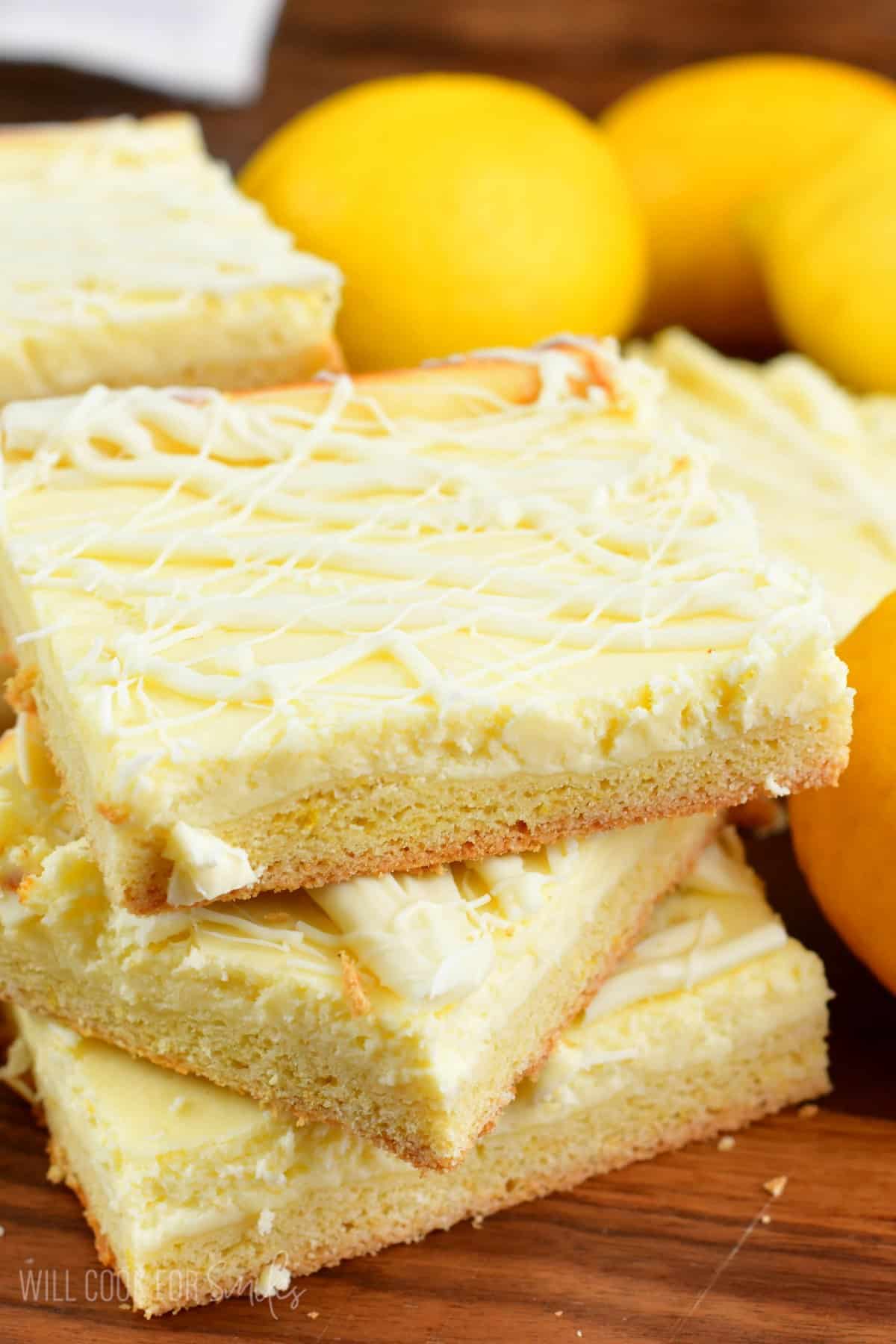 Lemon Cheesecake Cookie bars stacked up on top of each other on a wood cutting board.