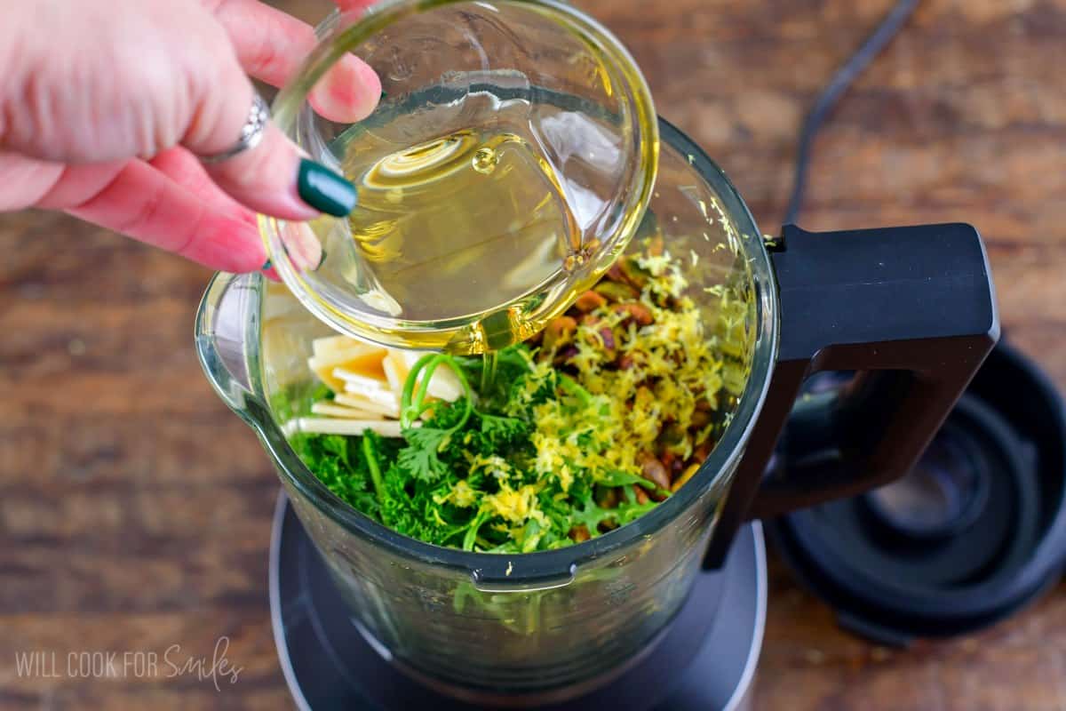 Adding oil to the pesto ingredients in a blender.