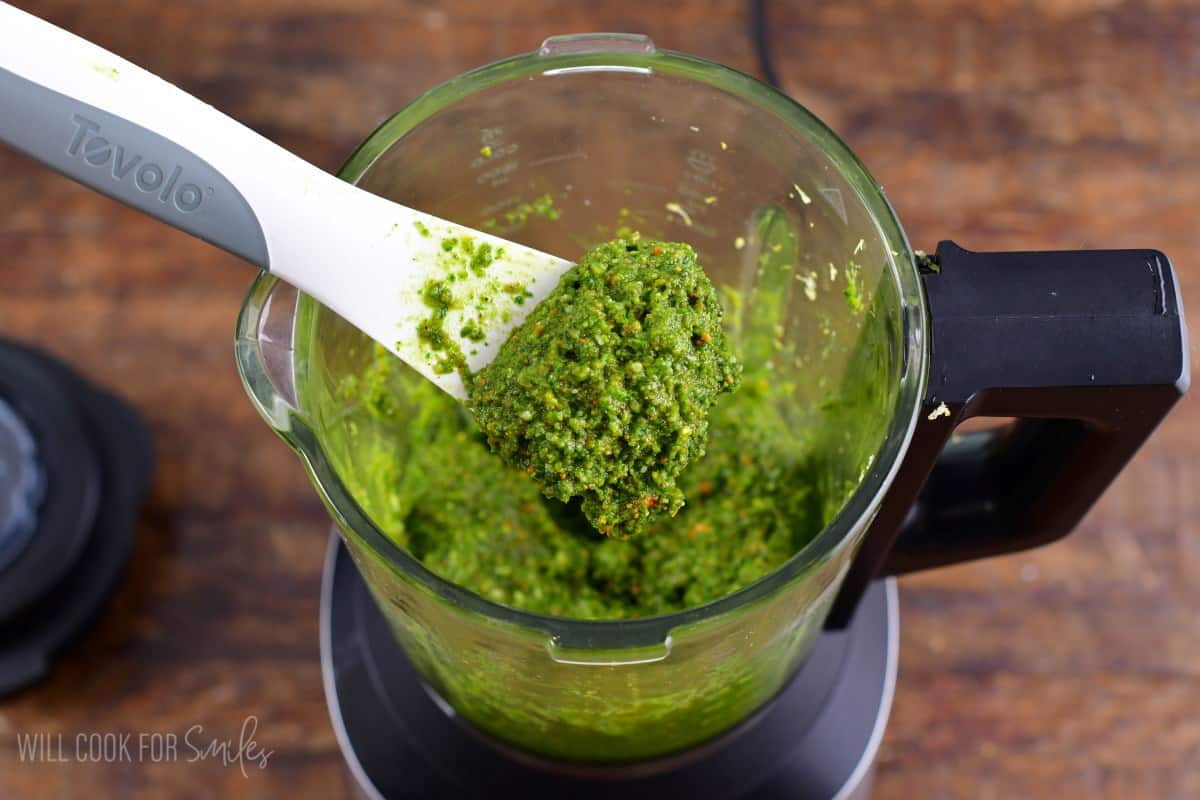 Scooping pesto out of the blender with a plastic spoon.