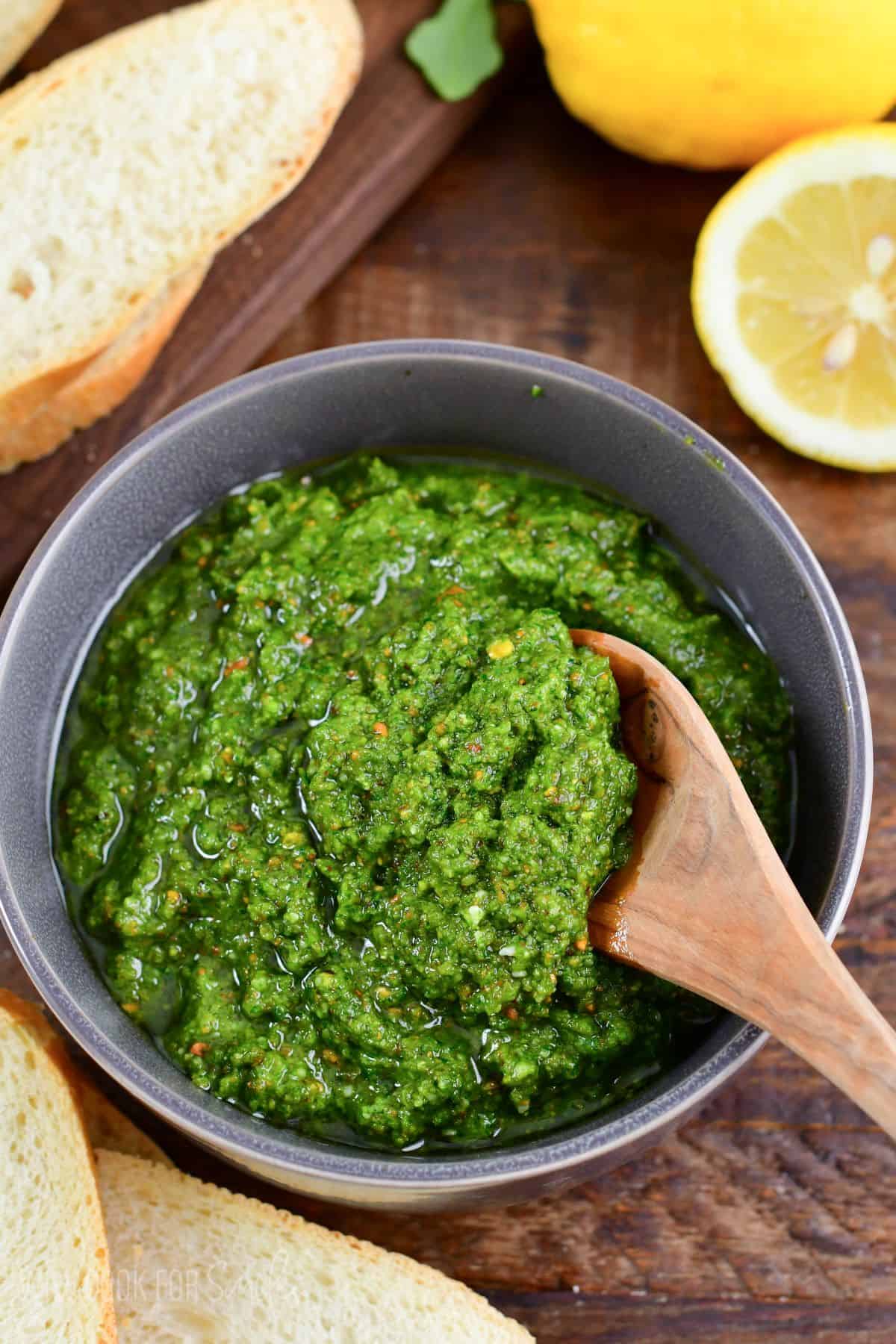 scooping Lemon Pistachio Arugula Pesto out of a bowl with a wooden spoon.