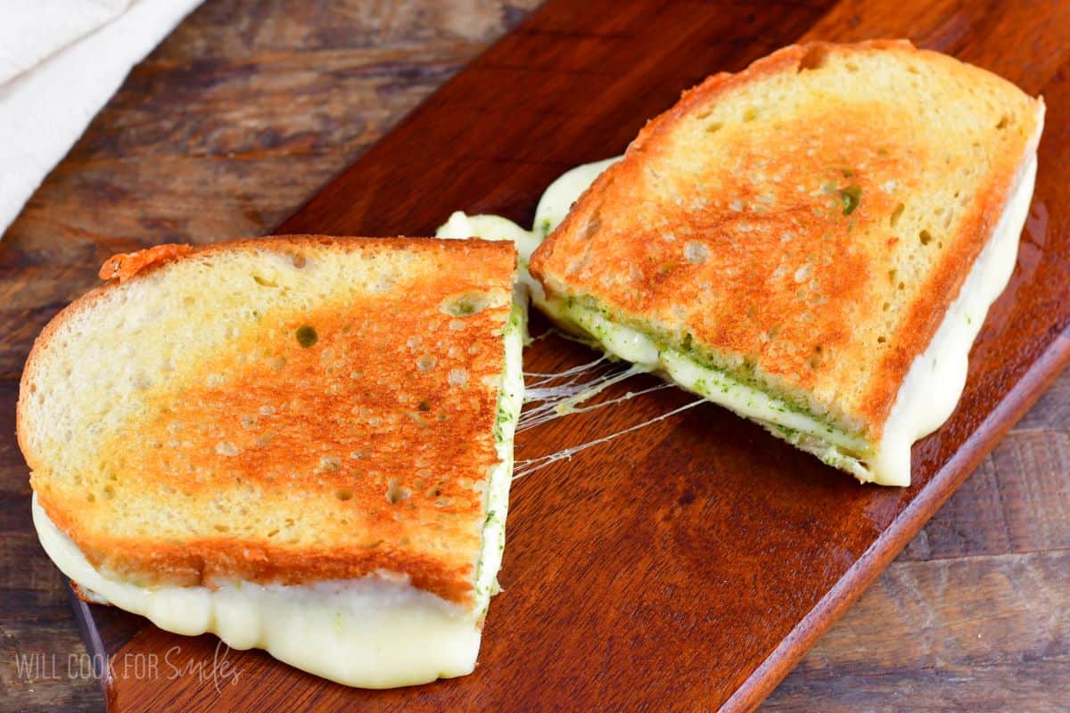 Pesto grilled cheese cut in half on a wood surface.