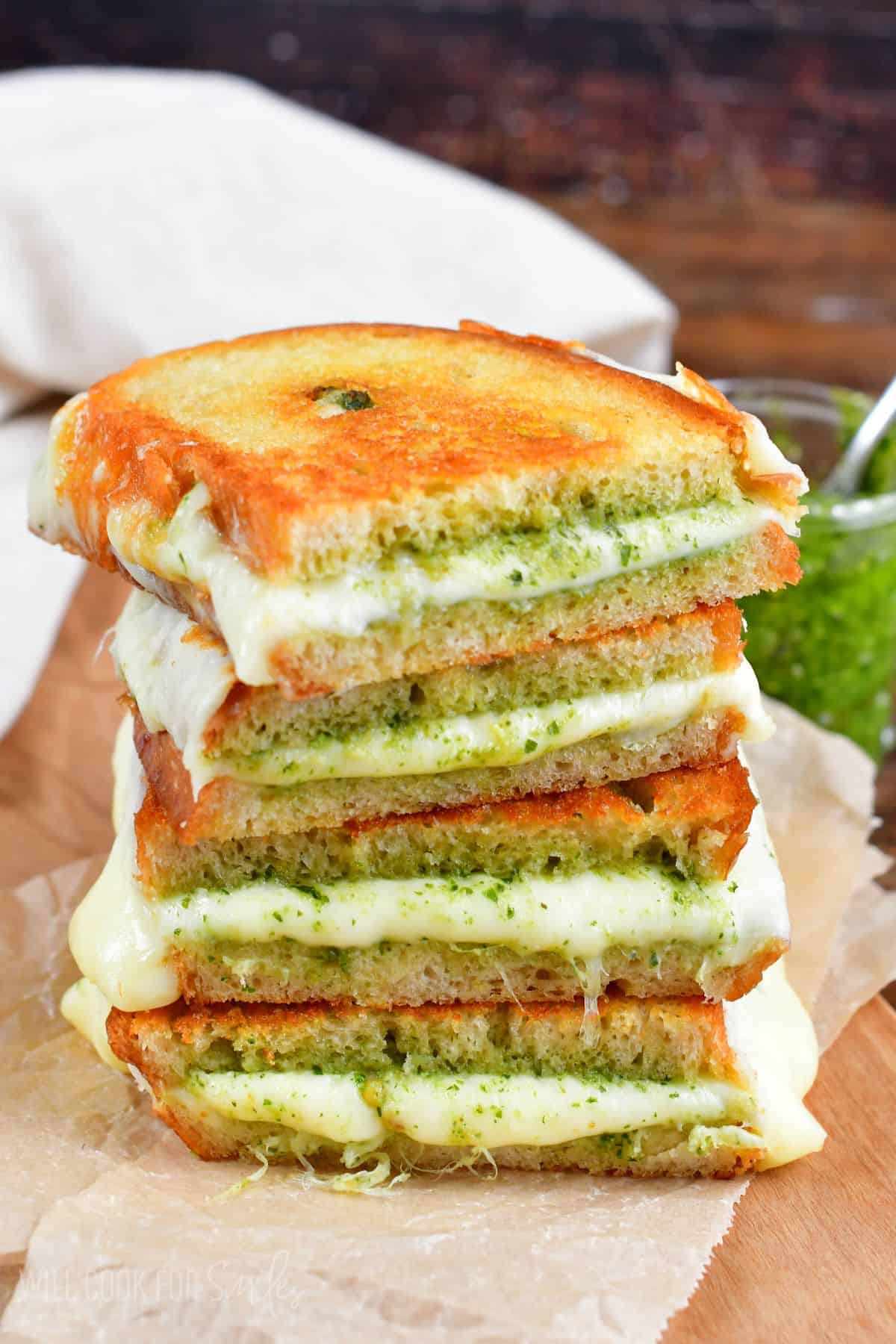 two pesto grilled cheese sandwiches cut in half and stacked up on a piece of parchment paper.