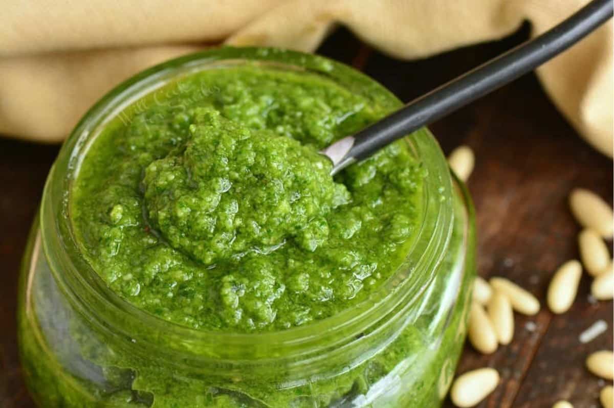 some pesto scooped on a metal spoon over the jar filled with basil pesto.