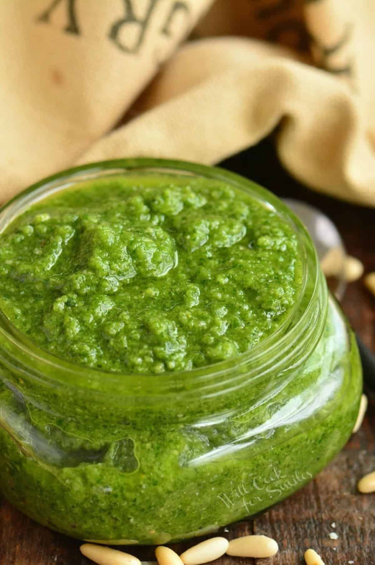 pesto filled to the top of a glass jar with some pine nuts on the table.