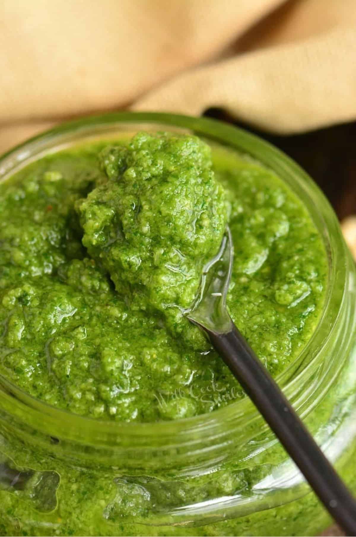 scooped pesto spooned on the metal spoon on top of the jar.