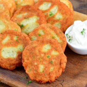 Potato pancakes on a wood cutting board with a bowl of sour cream to the side.