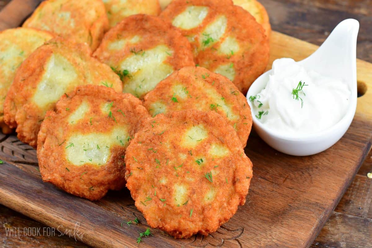 Potato pancakes on a wood cutting board with a bowl of sour cream to the side.