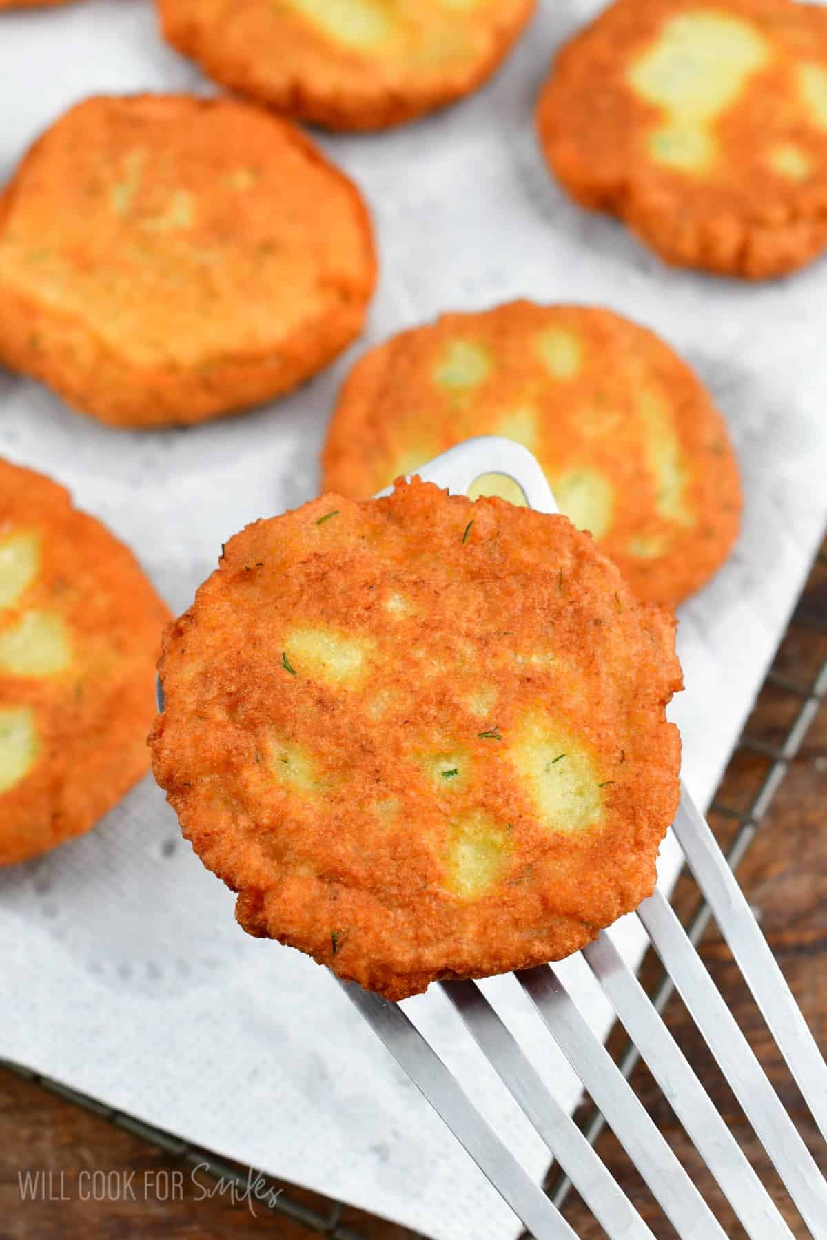 Potato Pancakes on wire rack with paper towels over it and on a spatula.