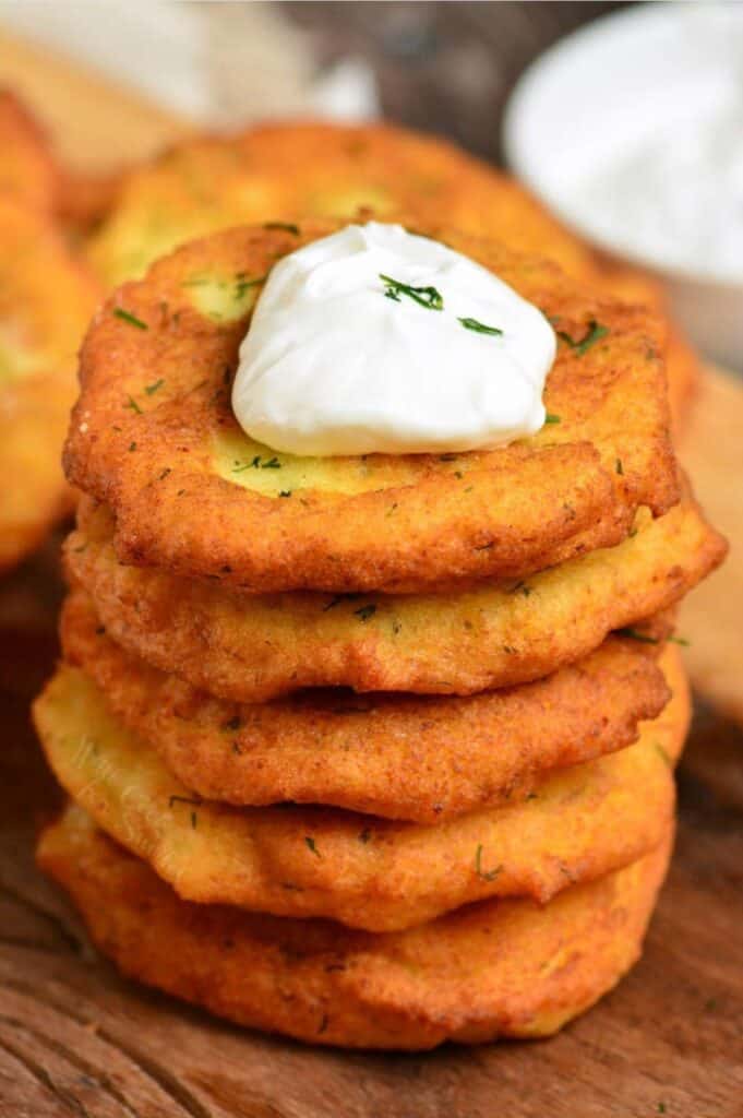 stacked of potato pancakes with a dollop of sour cream on top on a wood surface.
