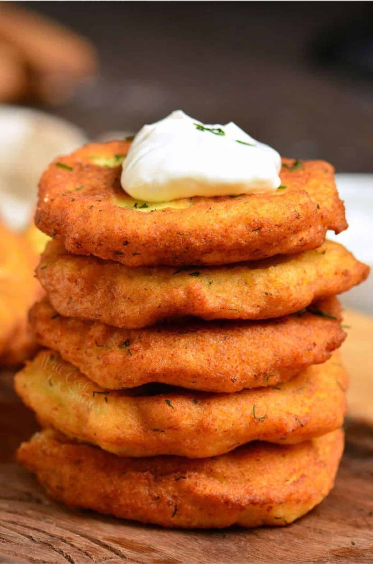 Potato pancakes on stacked on a wood surface with a dollop of sour cream on top.