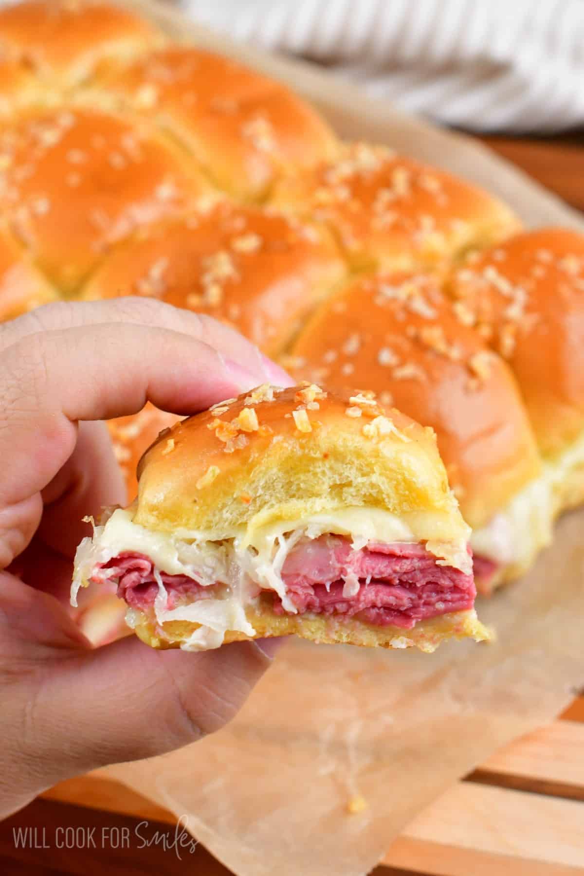 Holding a reuben slider while the rest of the sliders are in the background.