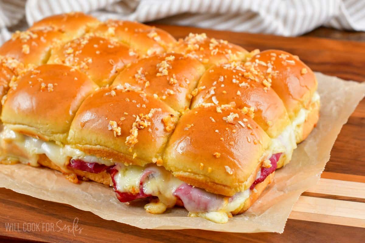 Baked Reuben sliders on a piece of parchment paper on a wood cutting board.