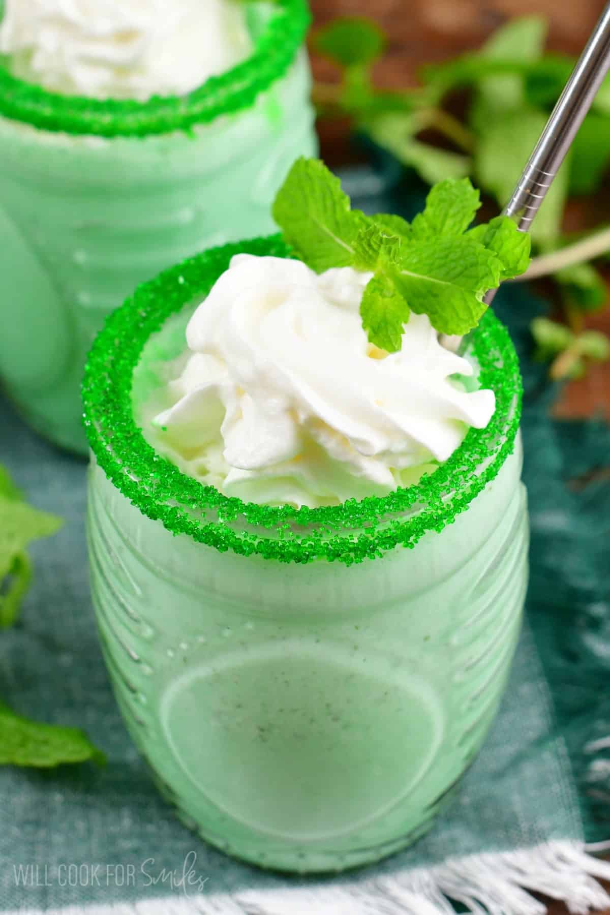 Shamrock shake in a glass with sprinkles on the rim of the glass and whipped cream and mint as garnish.