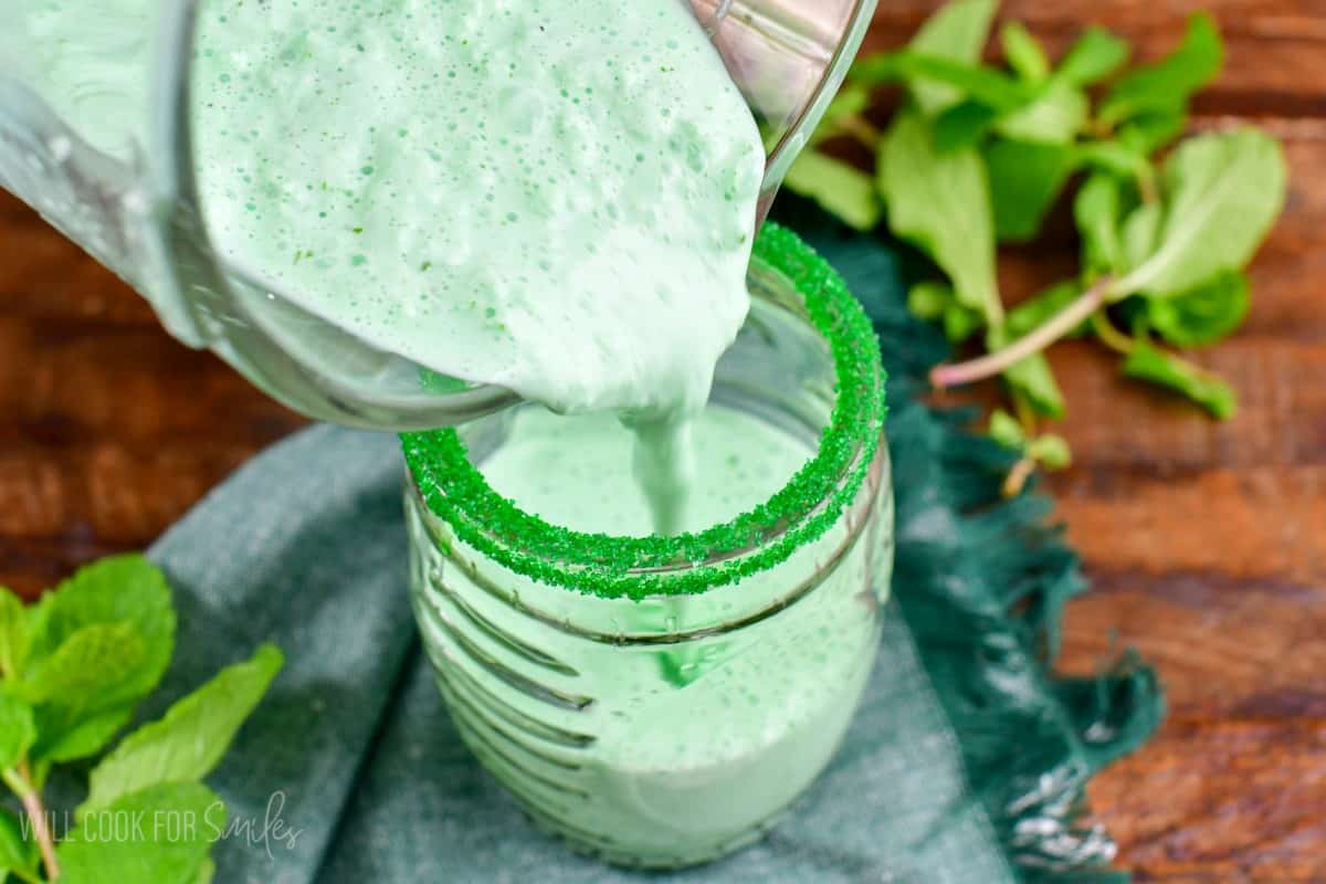 pouring shamrock shake into a glass rimmed with green sprinkles.