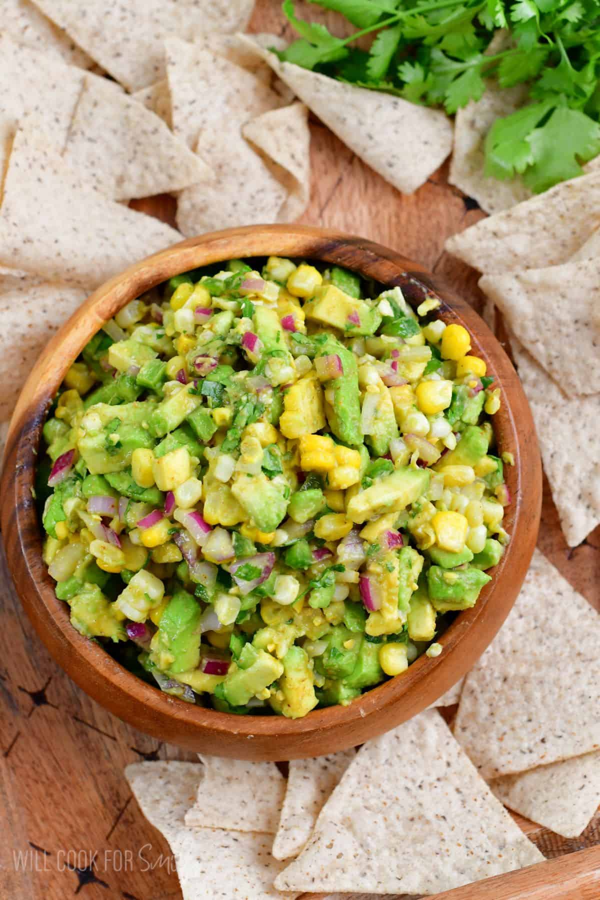 wood bowl of avocado salsa with tortilla chips around it.