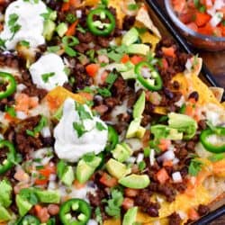 Beef nachos on a baking sheet on a wood surface.