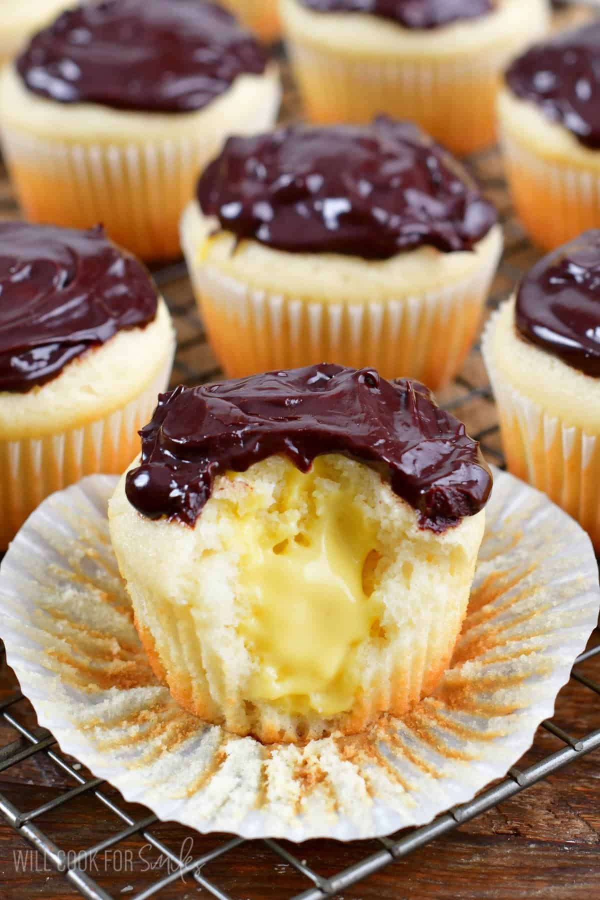 Boston cream donuts with a bite taken out on a wire rack with the cupcake wrapper taken off.