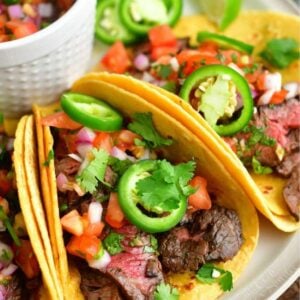 carne asada tacos topped with pico de gallo and jalapenos on a plate.