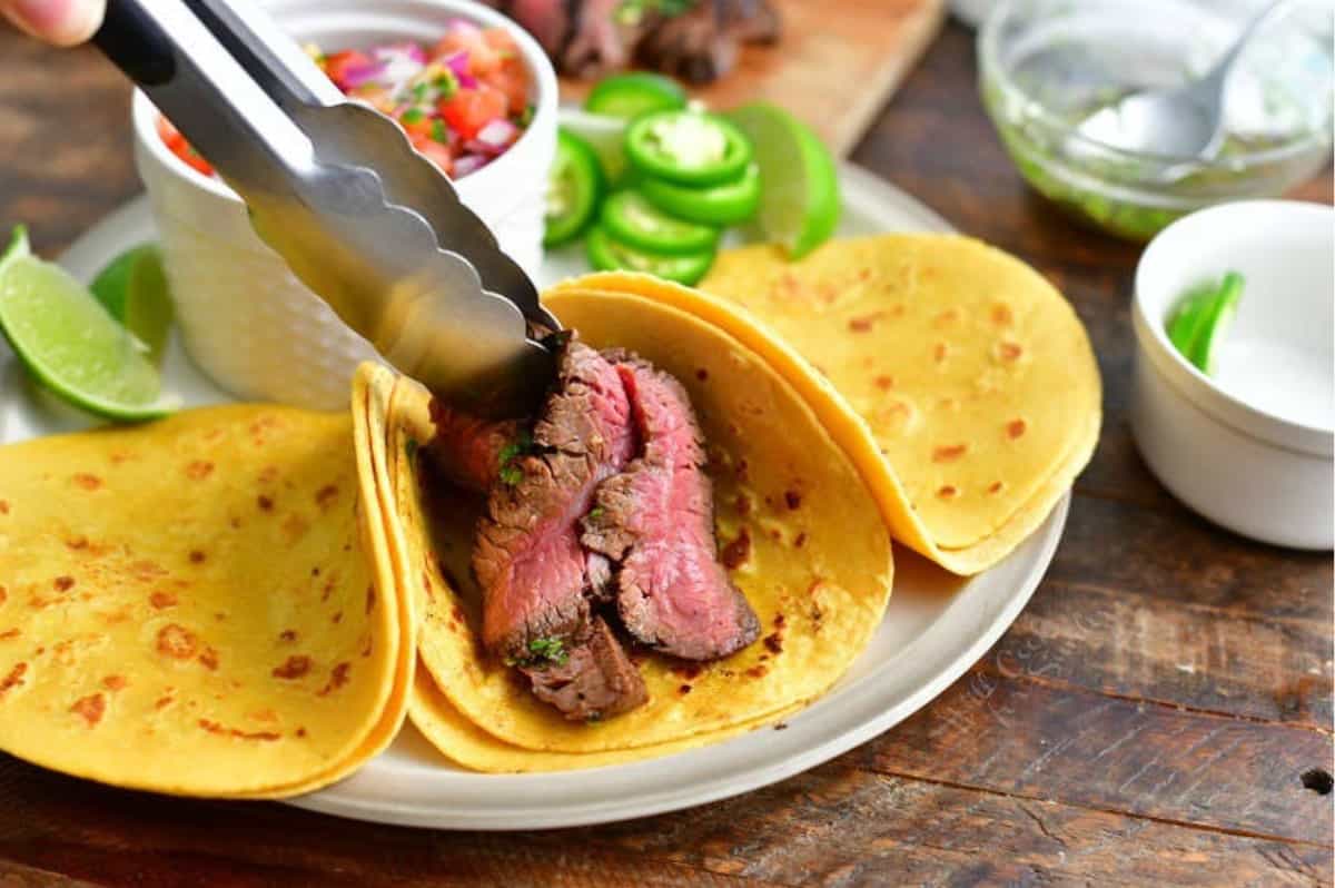 adding sliced steaks over into the taco shells to make the tacos.
