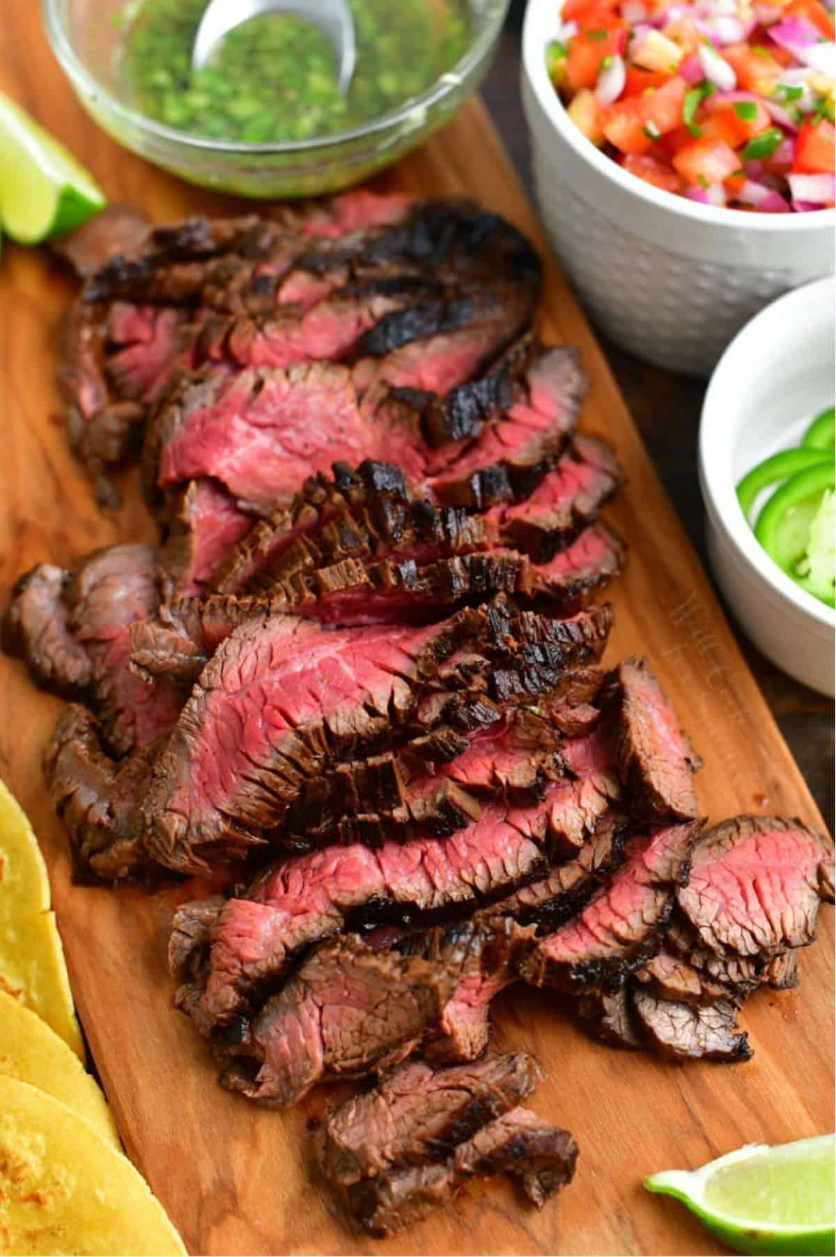 sliced carne asada next to topping on cutting board.