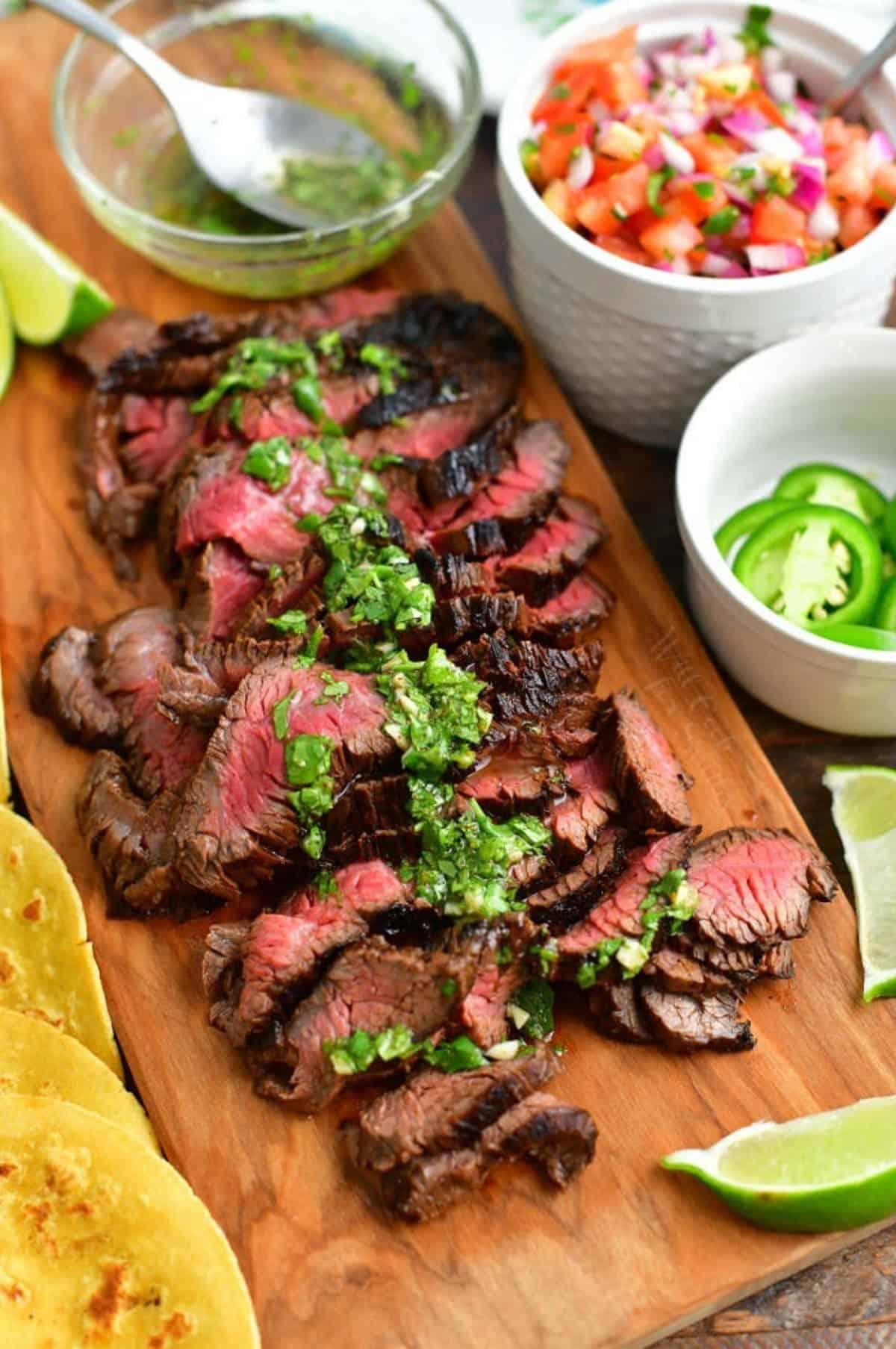 sliced carne asada topped with herb and citrus vinaigrette on cutting board.