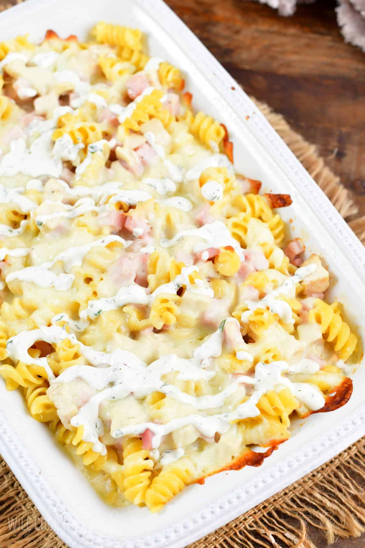 Chicken cordon bleu chicken casserole in a baking dish with ranch drizzled over top.