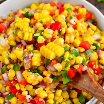 Corn salsa in a white bowl scooping some up with a wooden spoon.