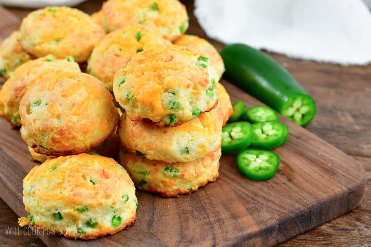 jalapeno cheddar biscuits stacked up on a cutting board with jalapeno slices to the right side.