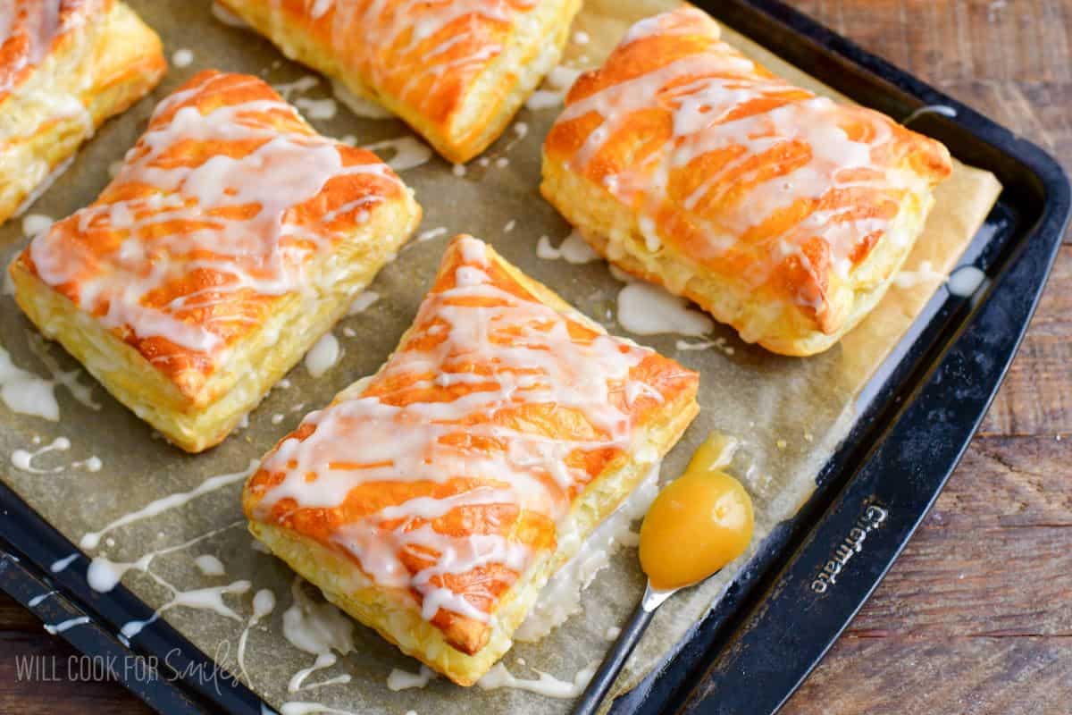 lemon cheesecake hand pies on a sheet pan with a spoon of lemon curd to the side.