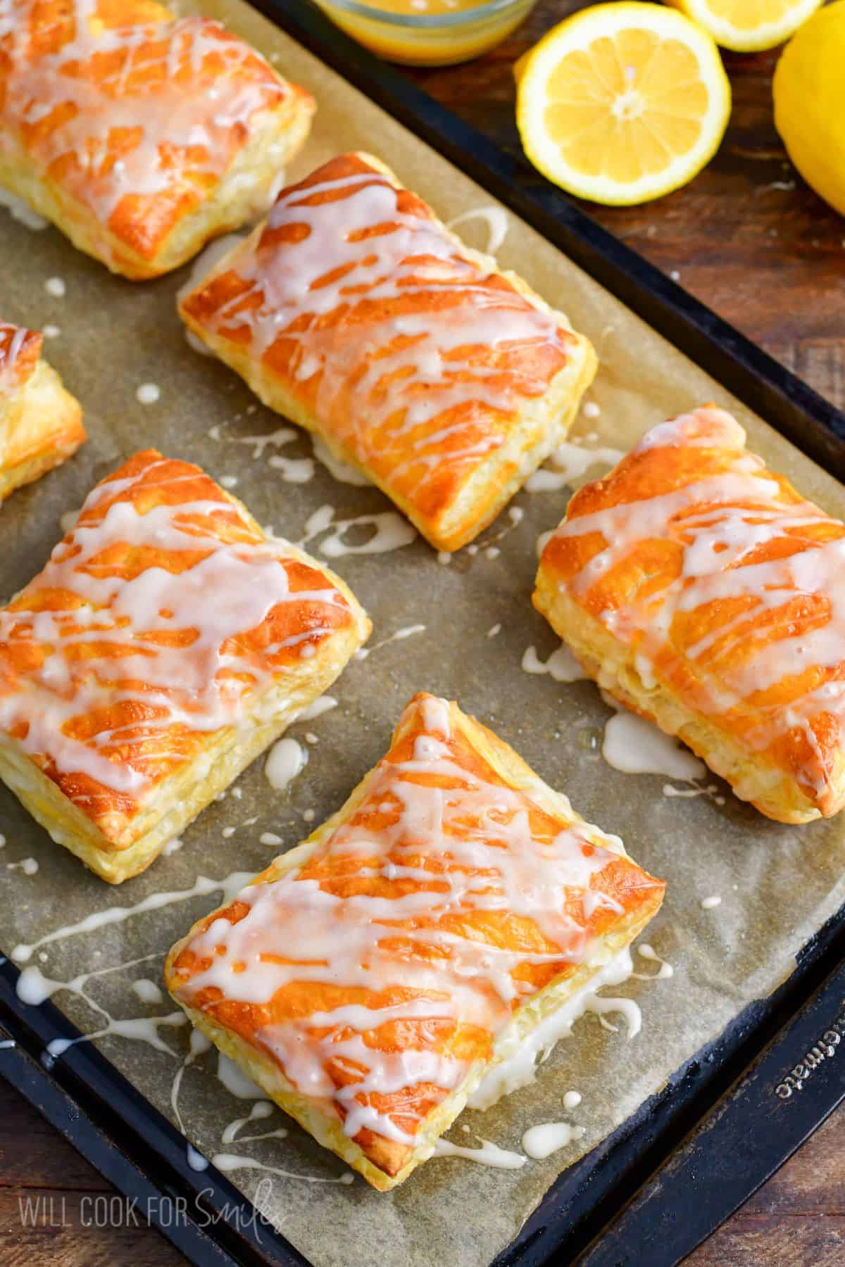 Lemon cheesecake hand pies on a baking sheet with icing on top.