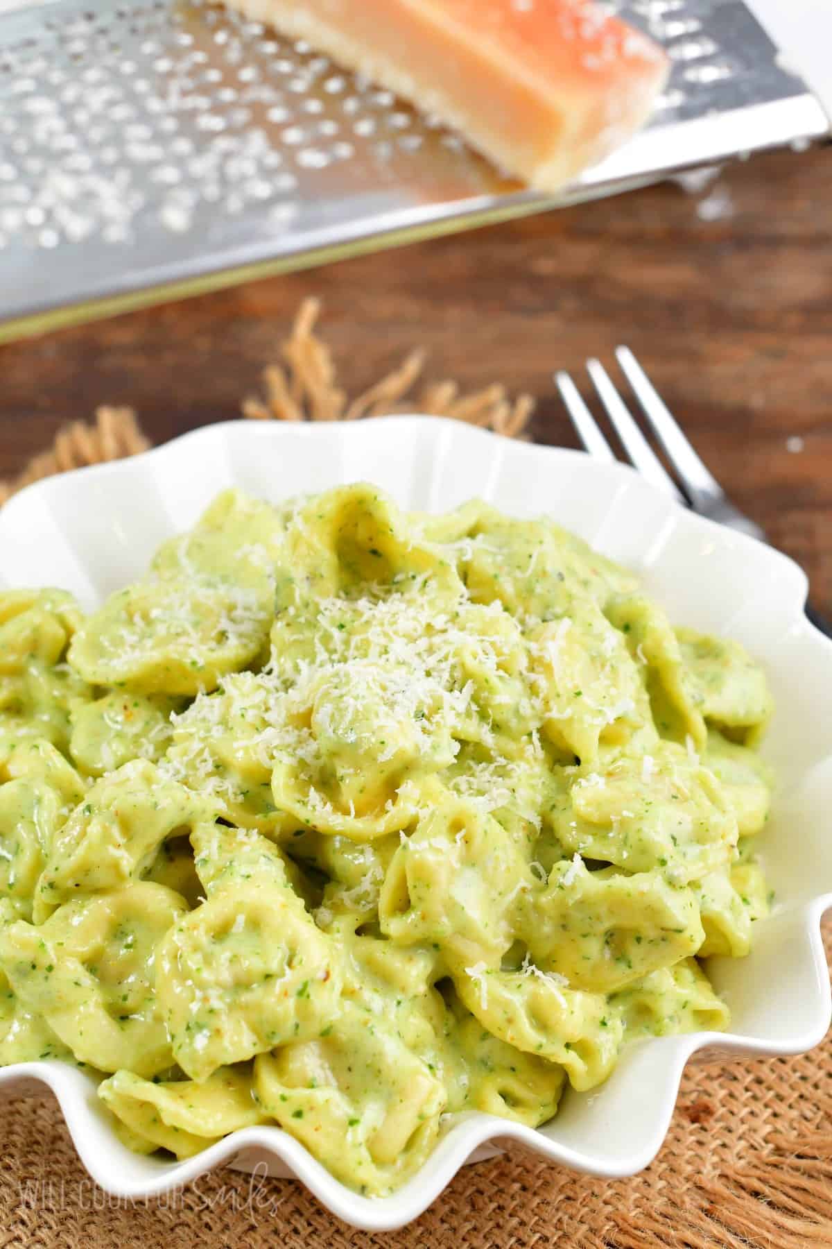 pesto alfredo tortellini in a bowl and adding parmesan cheese on top.