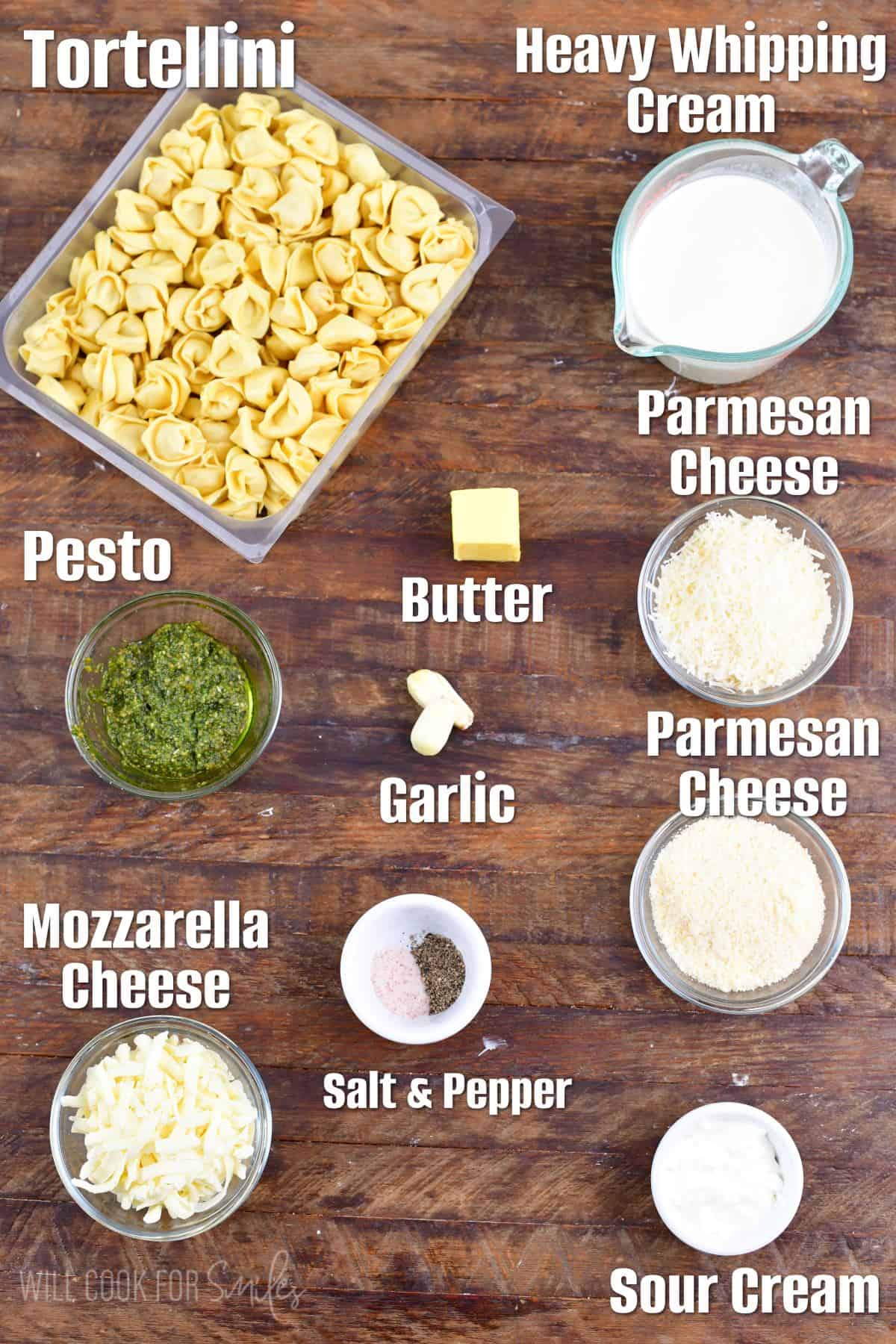 Labeled ingredients for pesto alfredo tortellini on a wood surface.
