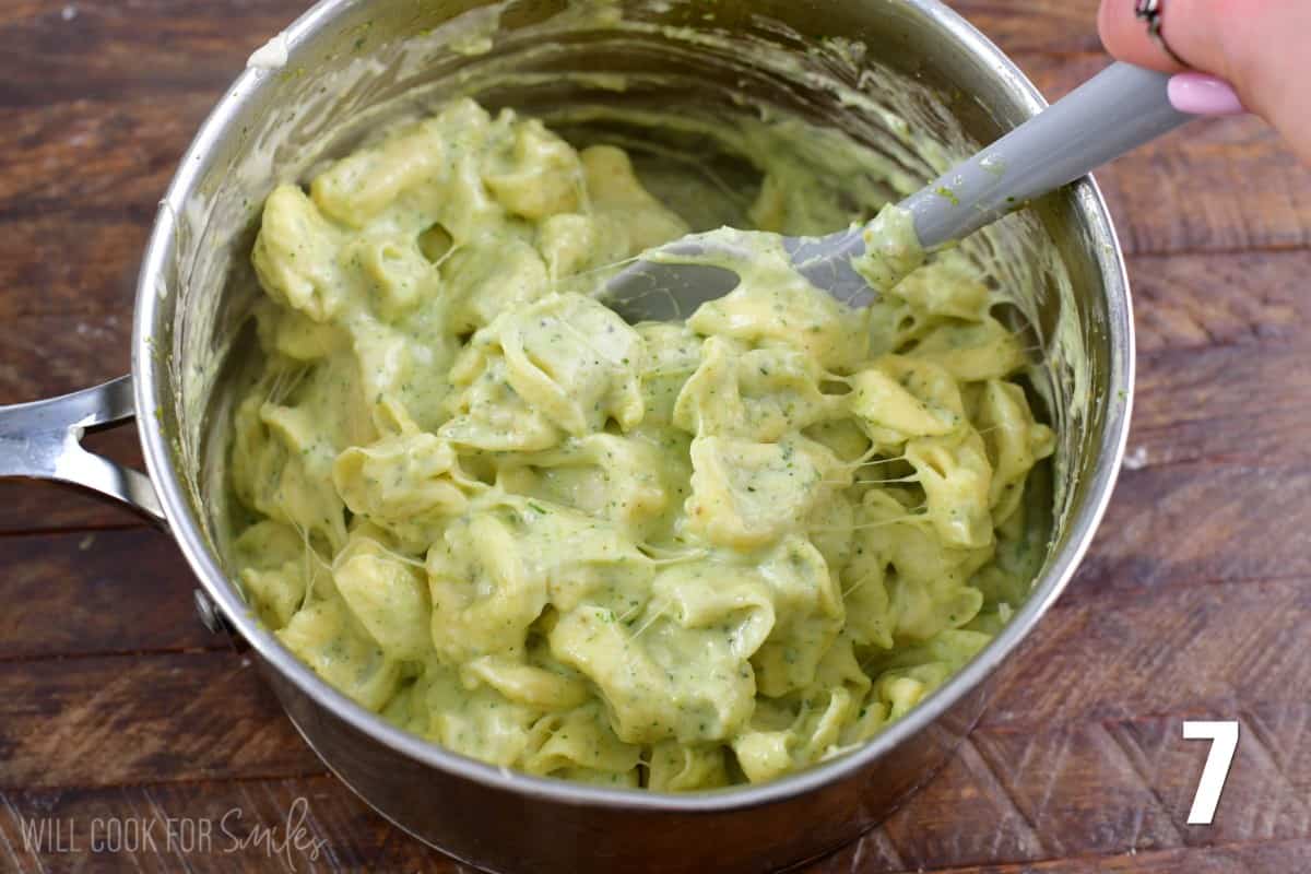 Mixing pesto alfredo in a pan with the tortellini with a plastic spoon.