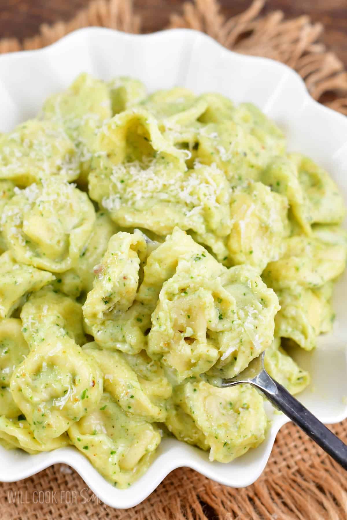 Pesto Alfredo Tortellini in a bowl scooped onto a fork.