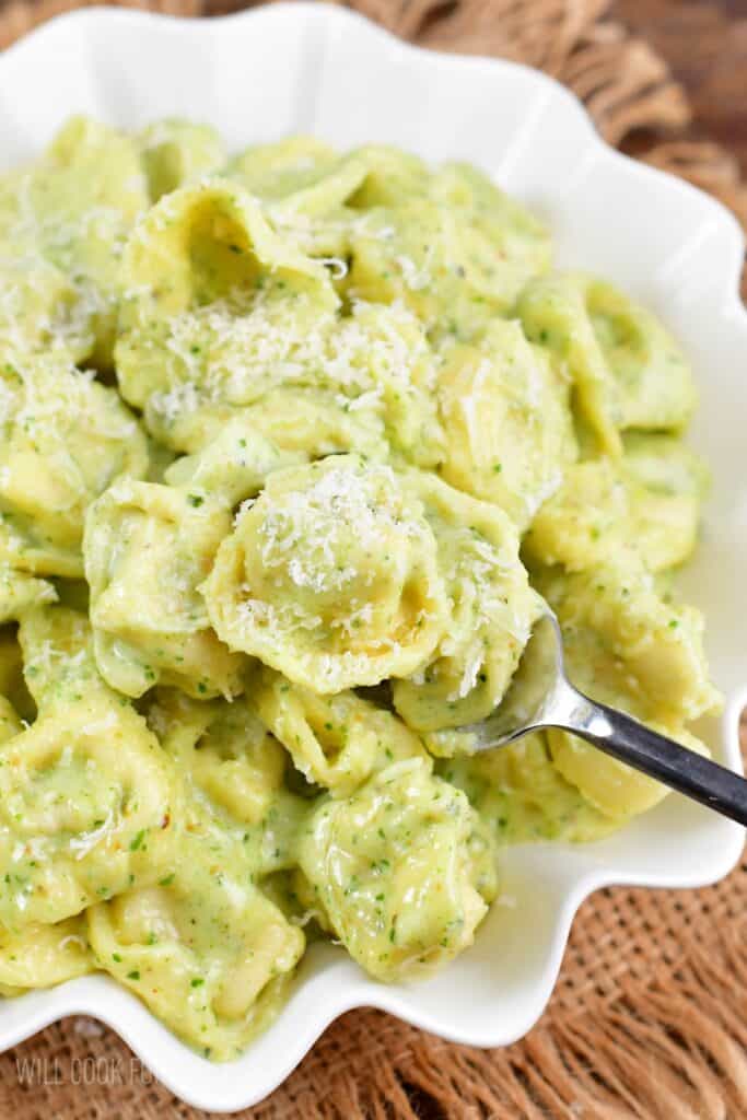 Pesto Alfredo Tortellini in a bowl scooping some of it up with a fork.