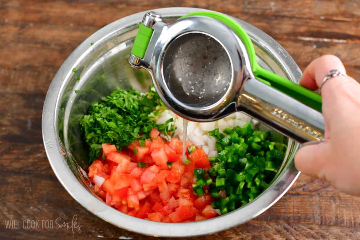 Squeezing lime into Pico de Gallo that is on a wood table.