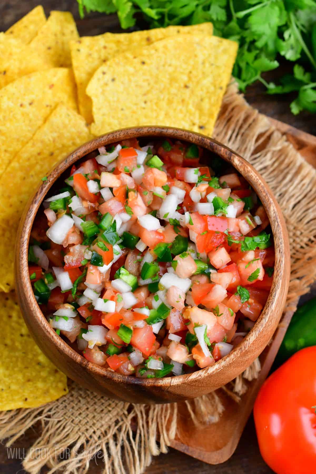Pico de Gallo in a wood bowl with tortilla chips to the left side.