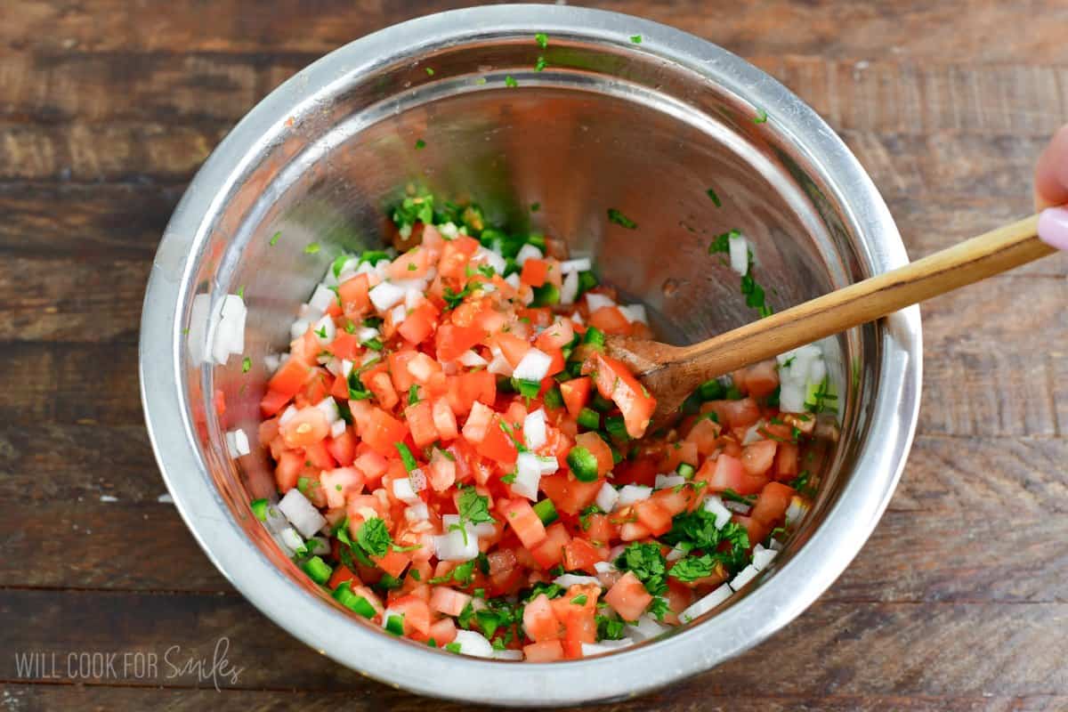 Stirring Pico de Gallo in a bowl with a wooden spoon.